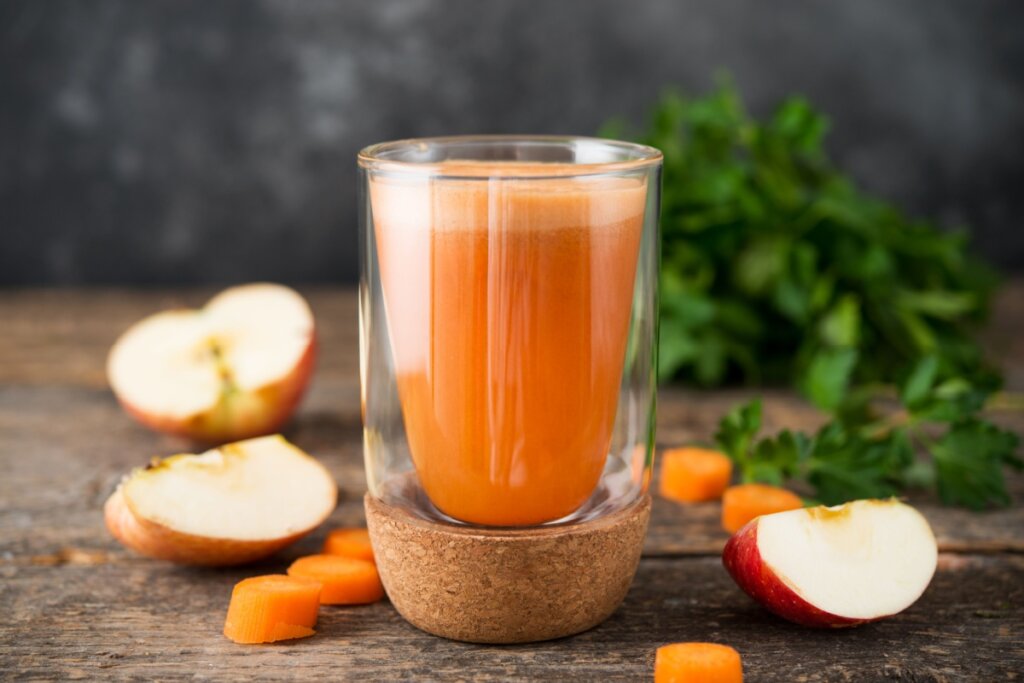 copo de vidro com suco de cenoura e maçã e ao redor na mesa, pedaços de maçã cortadas