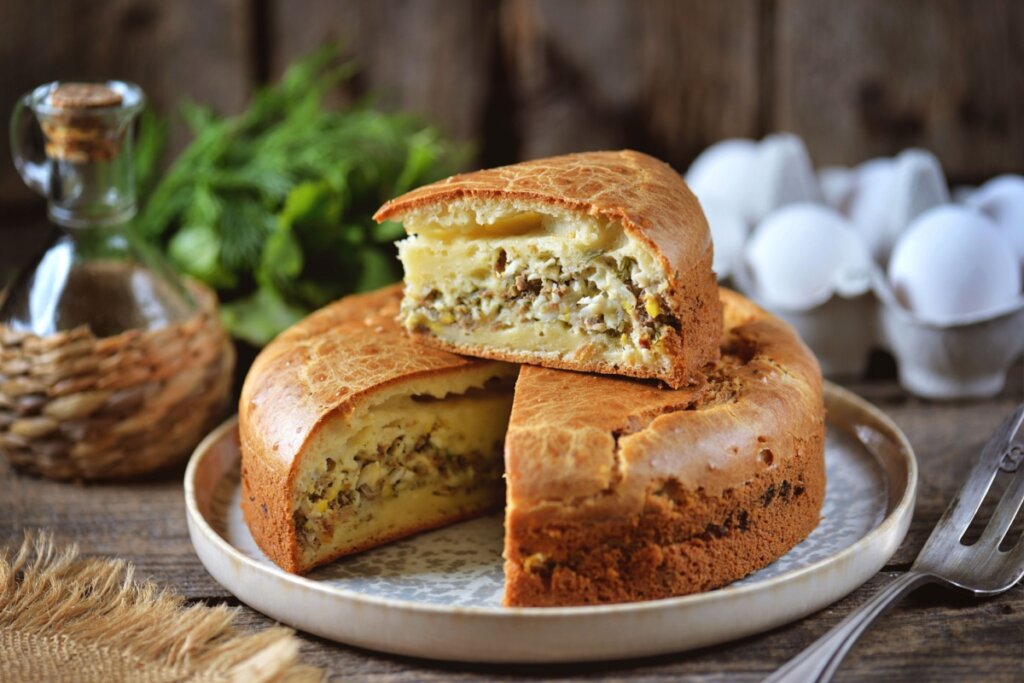 Torta de atum com ovo e cebola servida em prato branco em cima de mesa de madeira