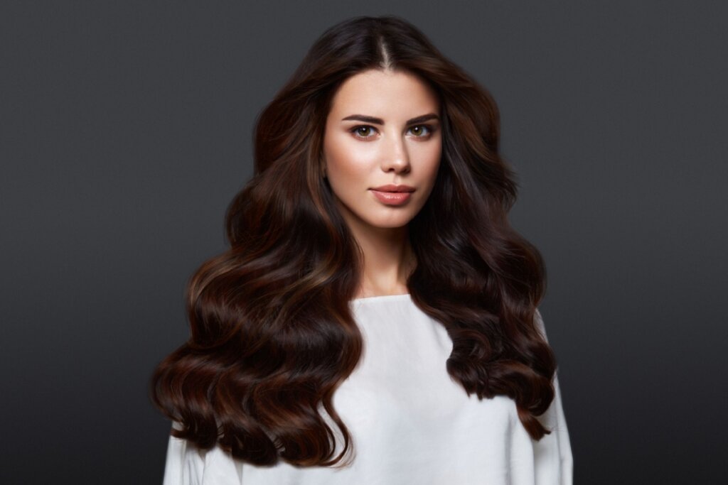 mulher de blusa branca e cabelo longo castanho e ondulado