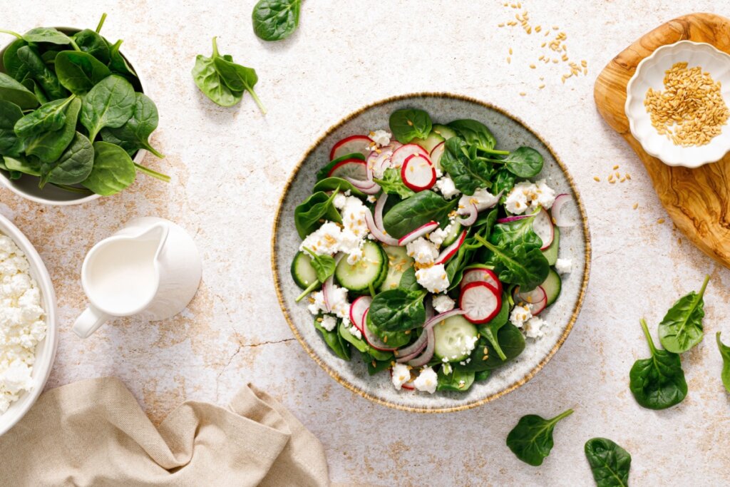 prato visto de cima com salada de espinafre com pepino, rabanete e queijo sobre superfície de mármore com folhas de espinafre