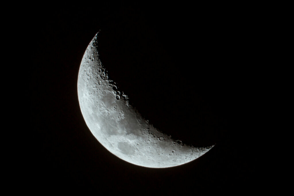 imagem da lua crescente, parcialmente iluminada, em céu escuro