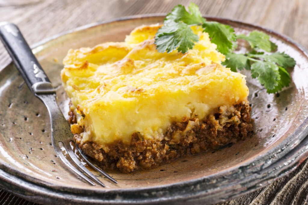 Escondidinho de carne moída em prato marrom com garfo 