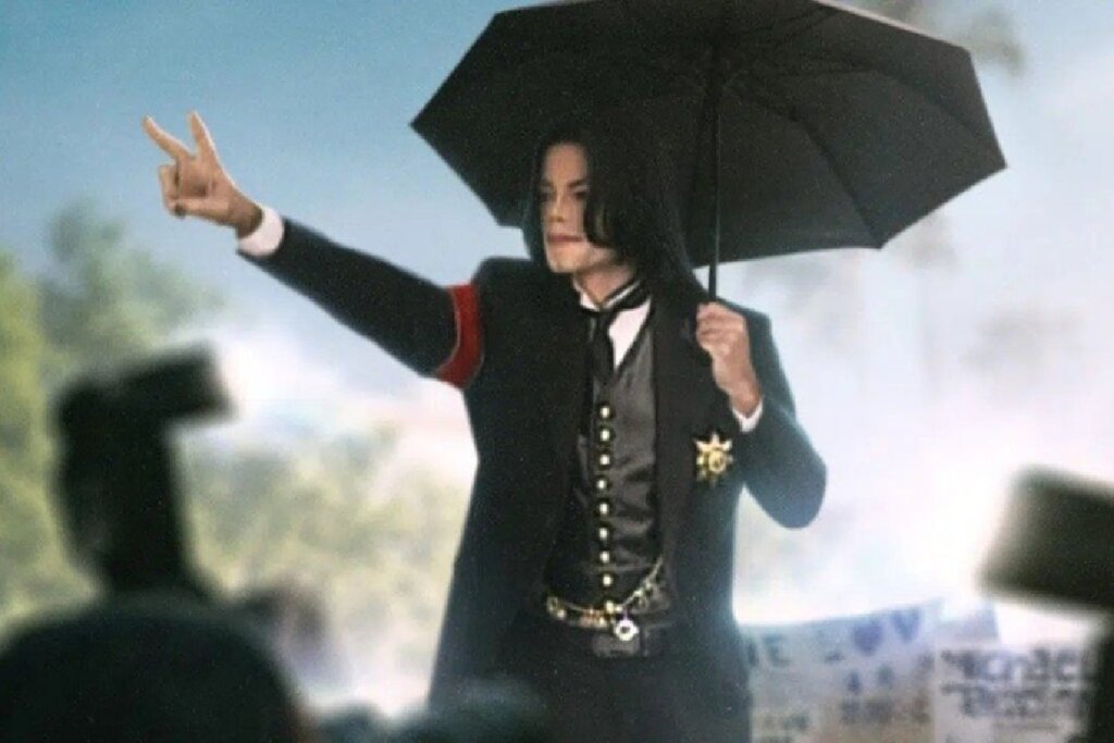 Foto de arquivo de Michael Jackson de terno sob a chuva, segurando um guarda-chuva preto e fazendo o sinal de paz com os dedos para a multidão.