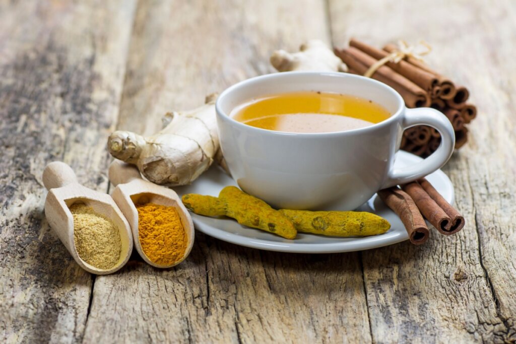 Chá de cúrcuma com gengibre e canela servido em xícara branca em cima de mesa de madeira