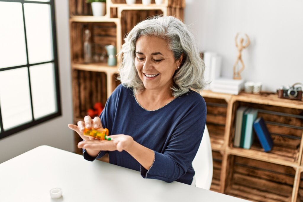 Mulher com cabelo curto, grisalho usando camisa azul sentada tomando remédio 
