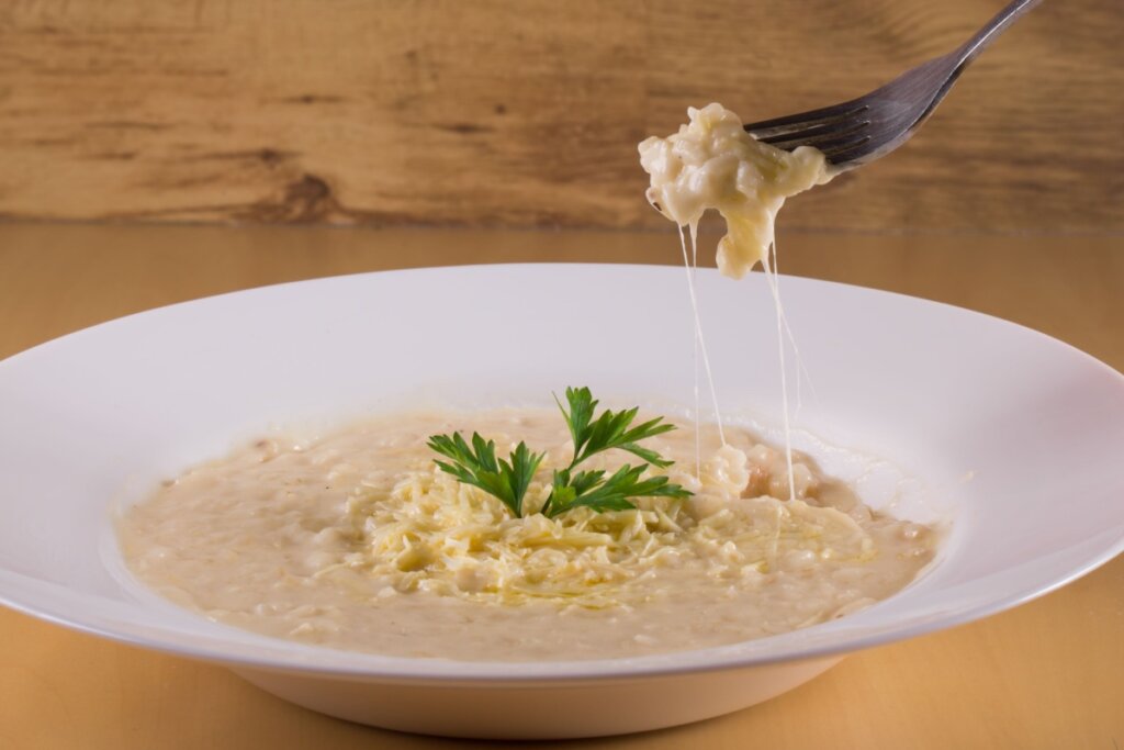 Prato branco com risoto de queijo e um garfo de metal acima 