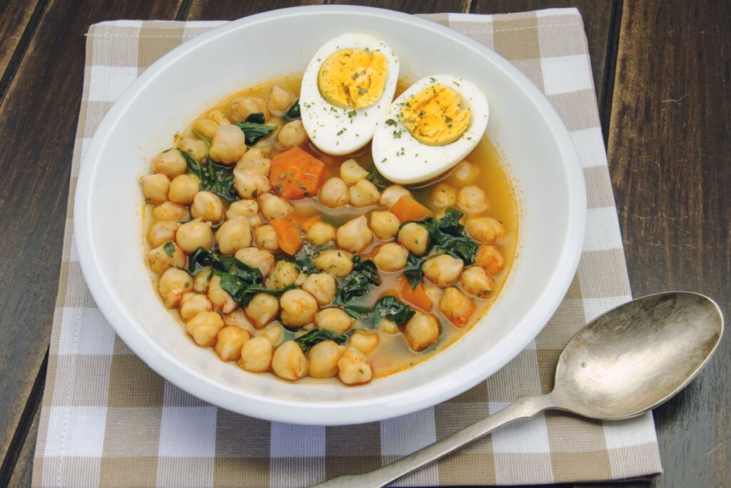 Prato branco com sopa de grão-de-bico com espinafre e ovo 