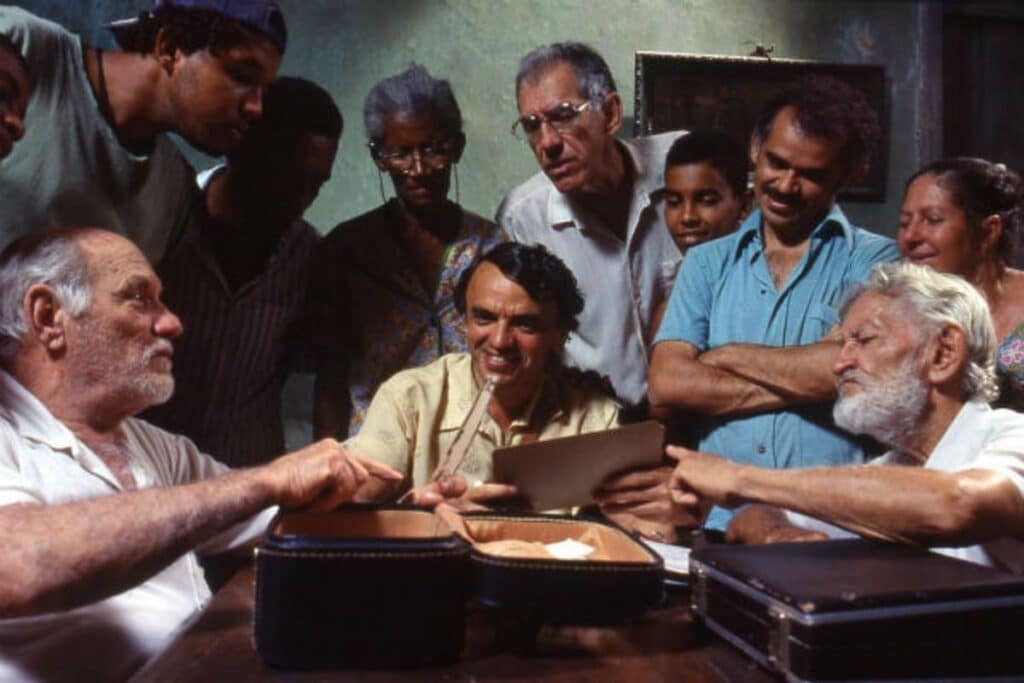 Personagens de "Narradores de Javé" reunidos ao redor de uma mesa e mexendo em um objeto