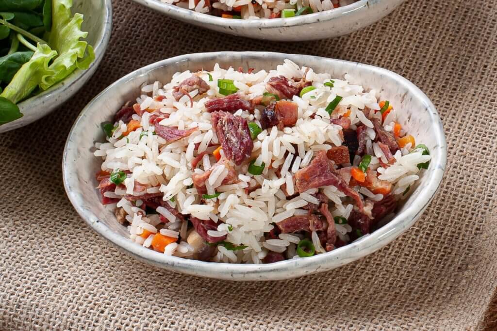 Arroz carreteiro servido em prato branco em cima de mesa de madeira