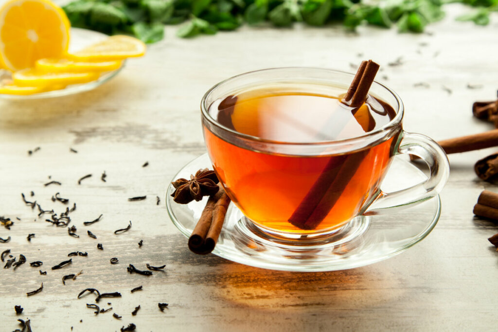Xícara transparente com chá de canela e canela em pau em cima de uma mesa de madeira