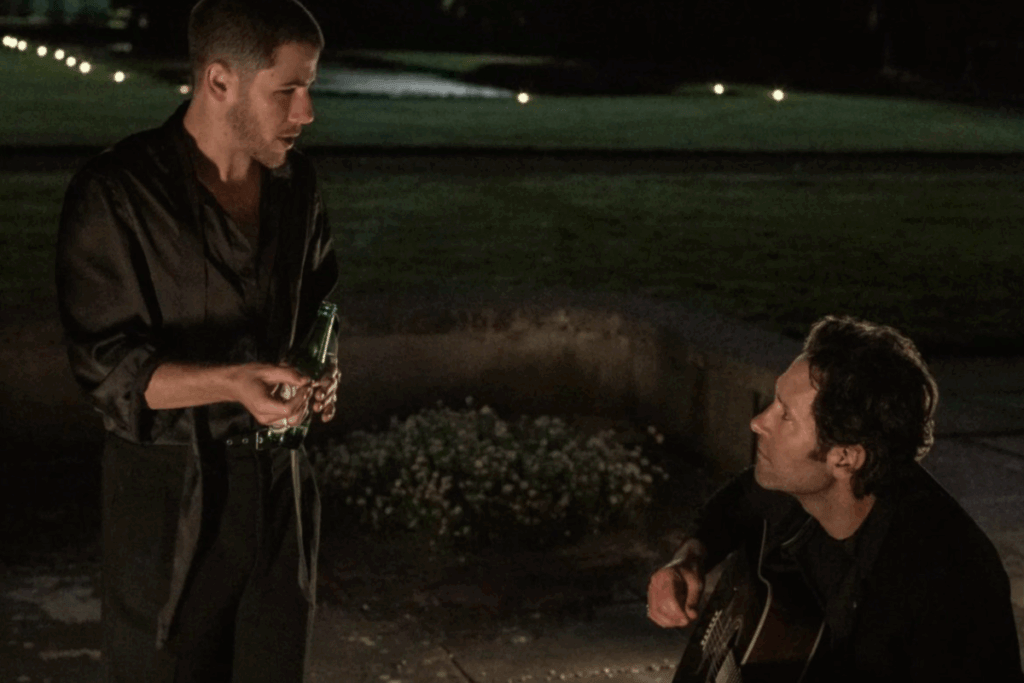 Dois homens conversando durante a noite, enquanto um deles toca violão
