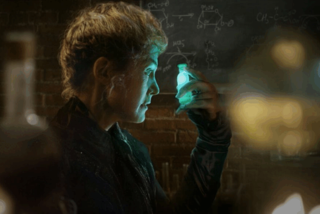 Mulher de perfil em um laboratório escuro, observando fixamente um pequeno frasco de vidro que emite uma intensa luz verde brilhante, com fórmulas químicas desenhadas em uma lousa ao fundo.