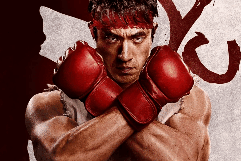 Um homem caracterizado como Ryu, com faixa vermelha na cabeça e luvas de combate vermelhas, olha seriamente para a frente com os braços cruzados em formato de "X" na altura do peito. O fundo tem tons avermelhados com elementos gráficos estilizados.