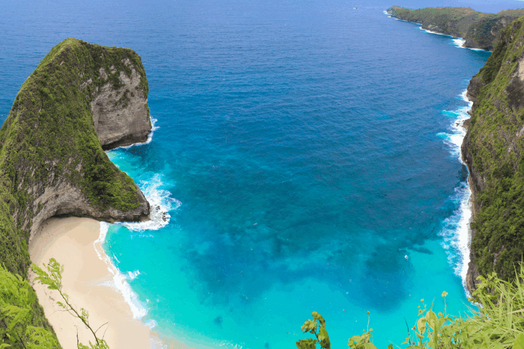 Vista do alto da praia de Kelingking, em Nusa Penida (Bali), com falésia verde coberta de vegetação sobre o mar azul-turquesa.